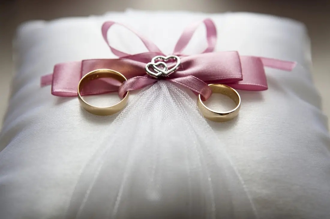 Gold wedding rings tied with ribbon on an ivory cushion